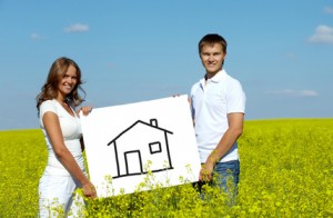 Un couple tient un cadre de tableau sur lequel est dessiné grossièrement une maison, avec des traits noirs. Cela peut représenter à la fois le crédit hypothécaire qu'ils comptent faire ou le crédit immobilier auquel ils voudraient souscrire.
