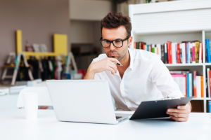 Un homme regarde pensivement son ordinateur portable, cherchant à faire une demande de credit en ligne ou de pret immobilier en ligne pour ses projets.